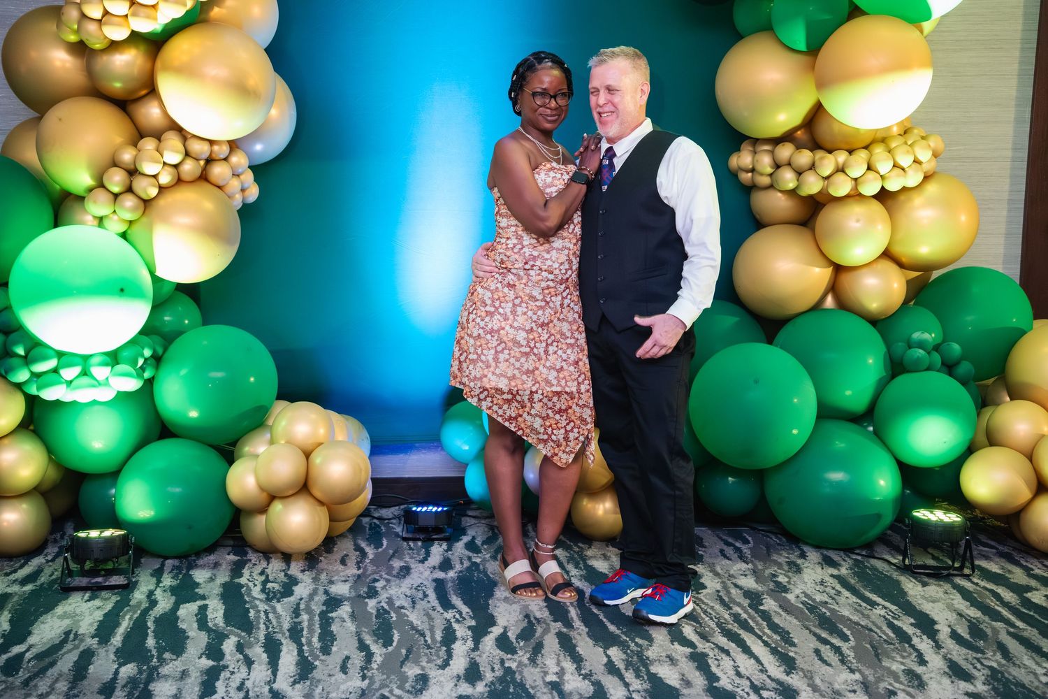 A festive balloon arch display featuring green and gold balloons against a blue-lit wall creates an elegant party atmosphere.