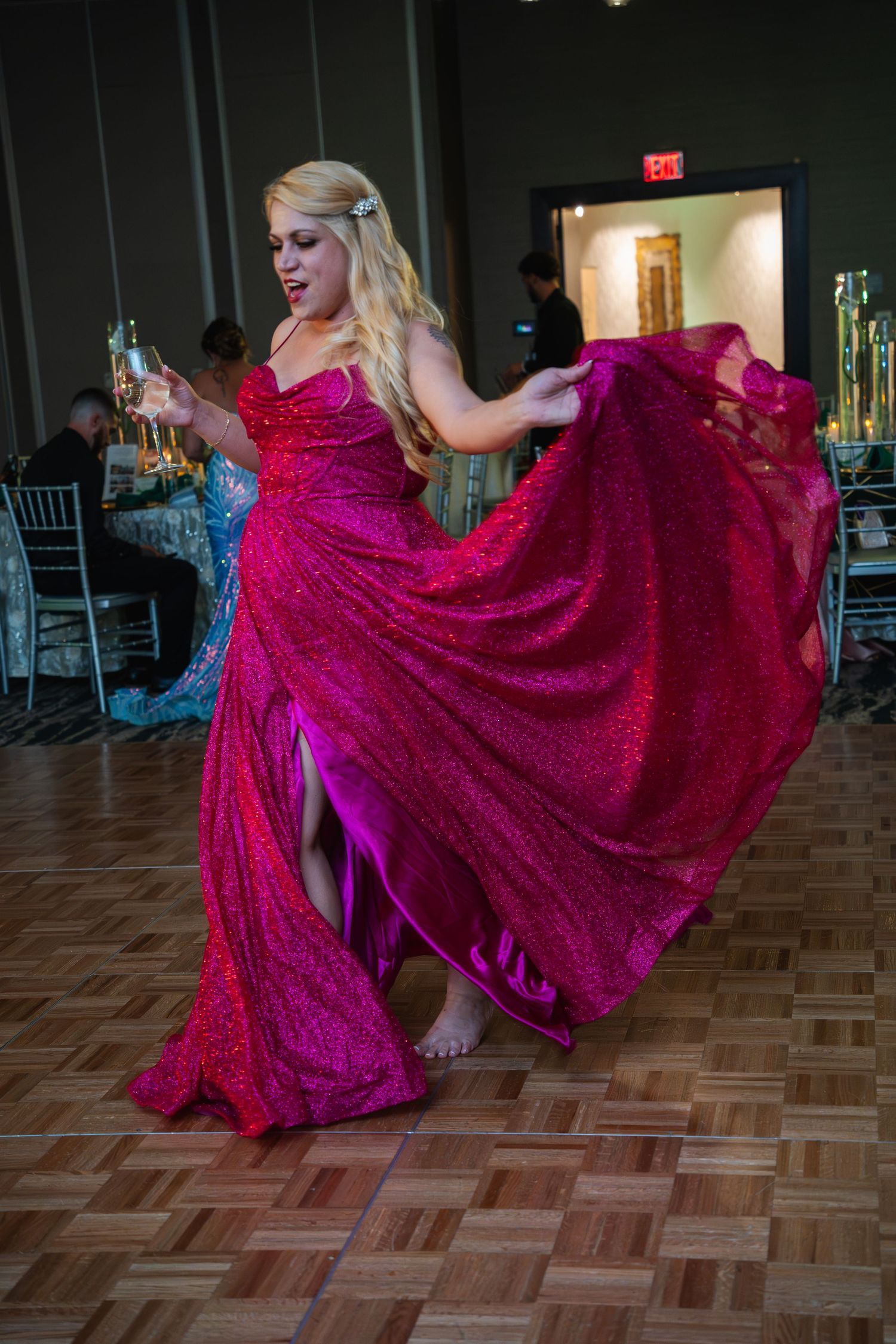 A dancer in a flowing magenta gown twirls gracefully across a parquet dance floor at an elegant event.