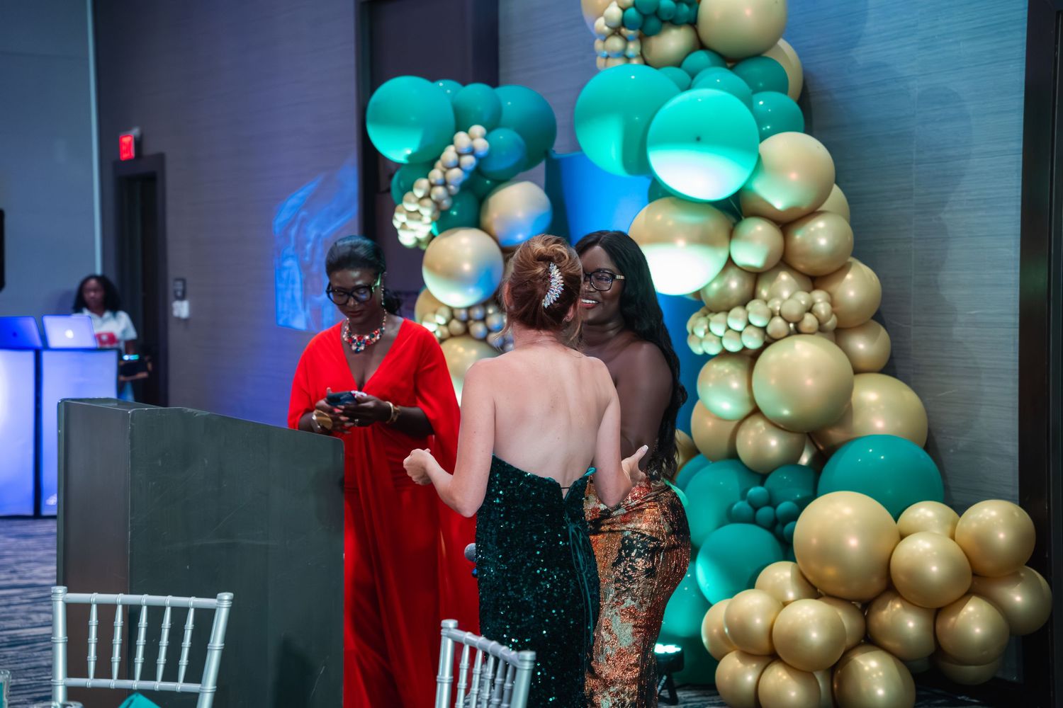 Event space decorated with elegant gold and teal balloon garlands against a modern blue-lit backdrop.