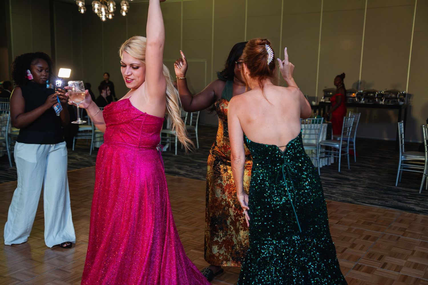 People dancing at a formal event with guests wearing pink and dark green evening gowns.