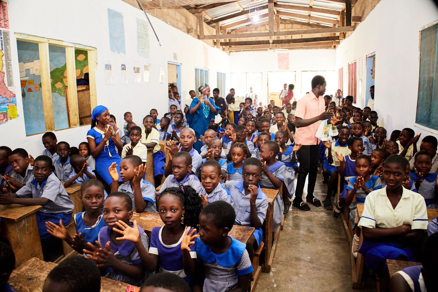 Students in blue uniforms sitting in rows at a covered outdoor learning area during class.