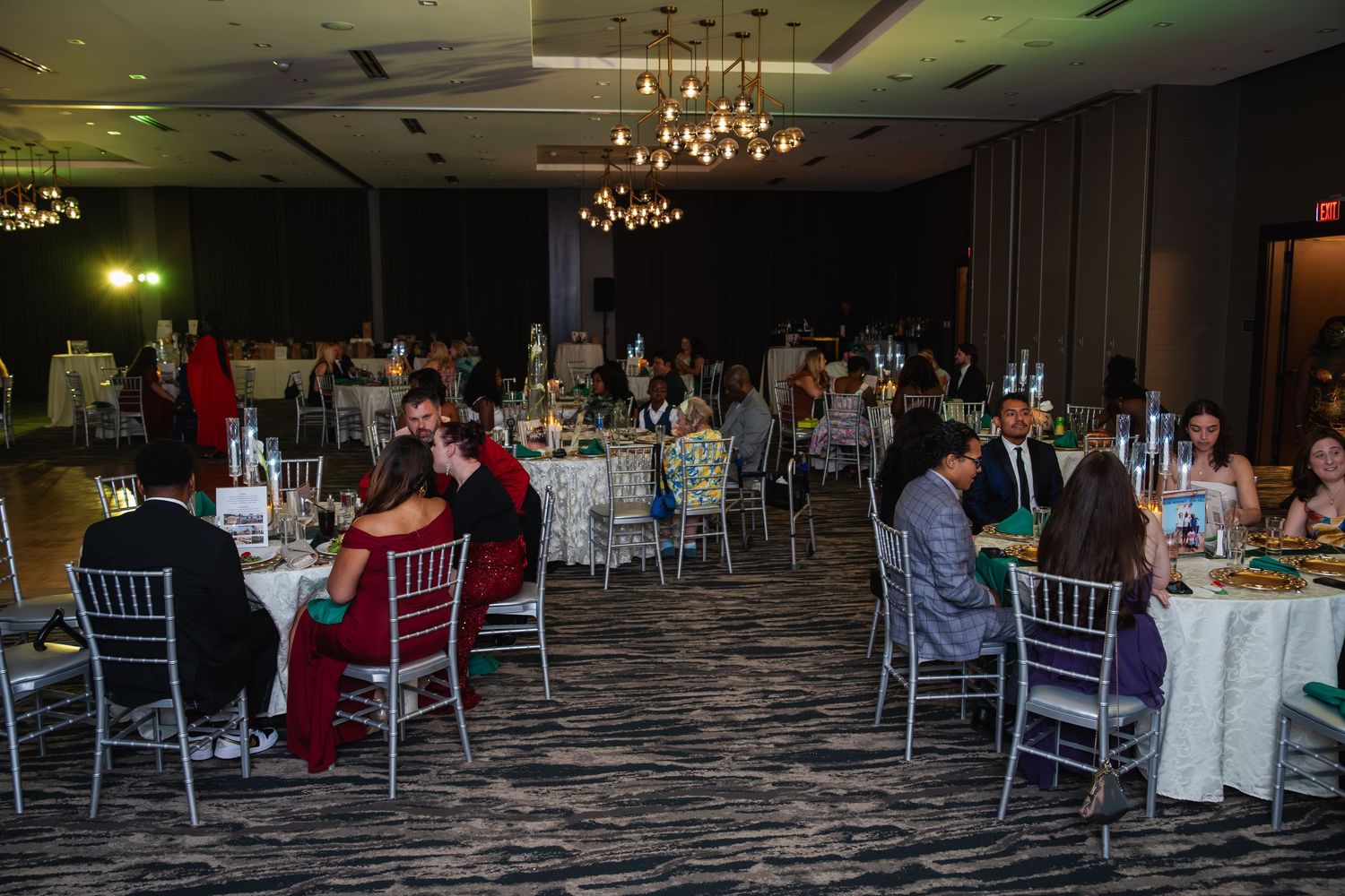 Panoramic view of an elegant wedding reception venue with chandeliers, white chairs and decorated tables.