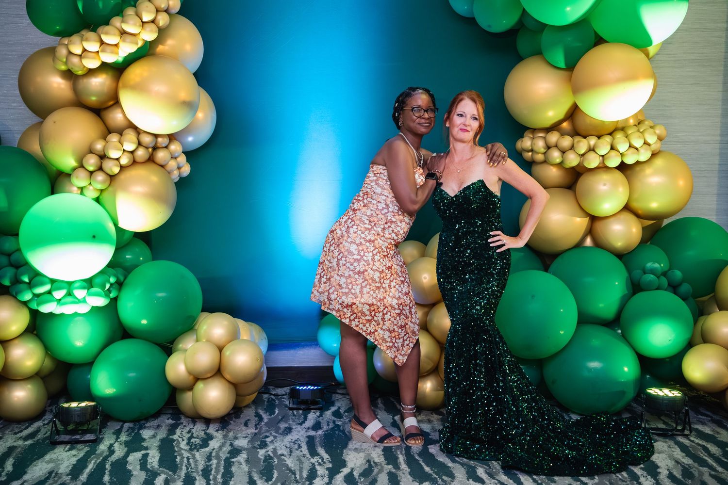 A decorative balloon arch installation featuring emerald green and metallic gold balloons with a blue background.