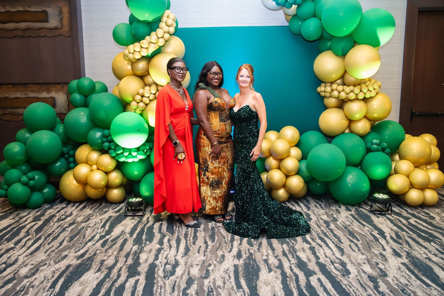 A festive party setup with green and gold balloon decorations against a teal wall backdrop.