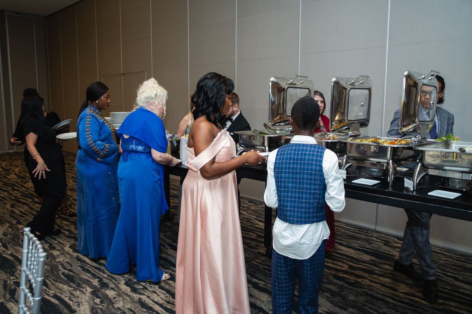 People in business attire gather around tables at a conference or meeting event in a hotel ballroom.
