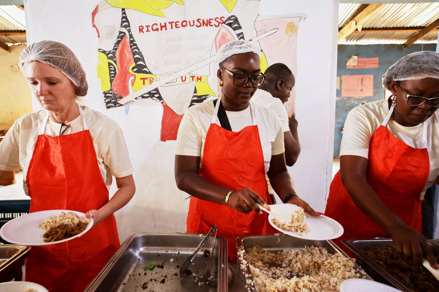 Food service workers in red aprons serving meals from a buffet line.