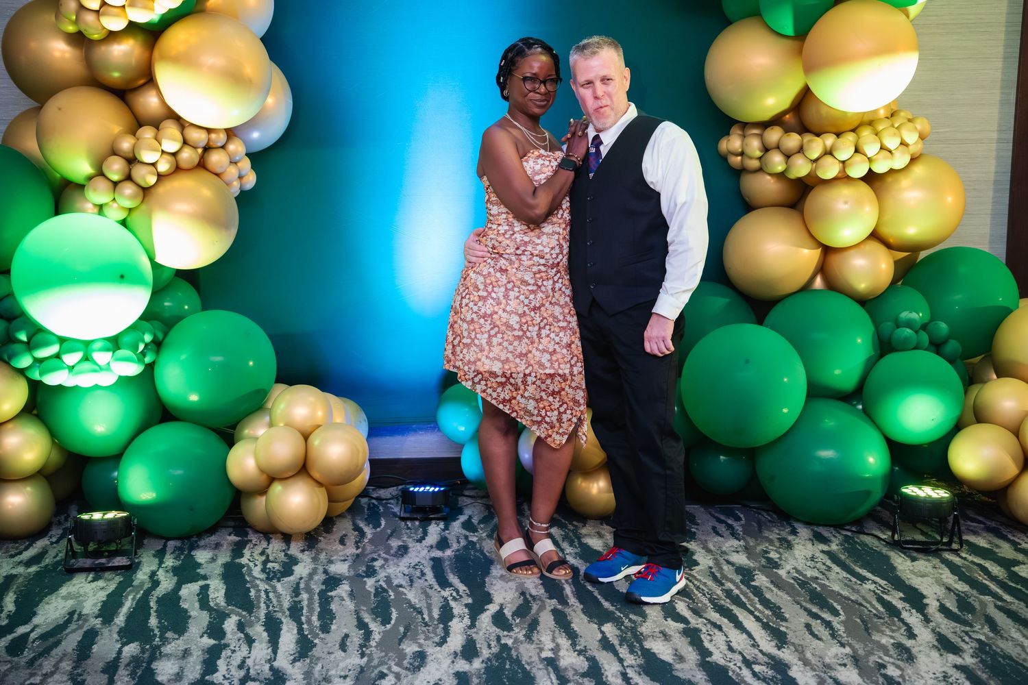 Festive balloon arch display featuring green and gold balloons against a blue wall creates an elegant party atmosphere.