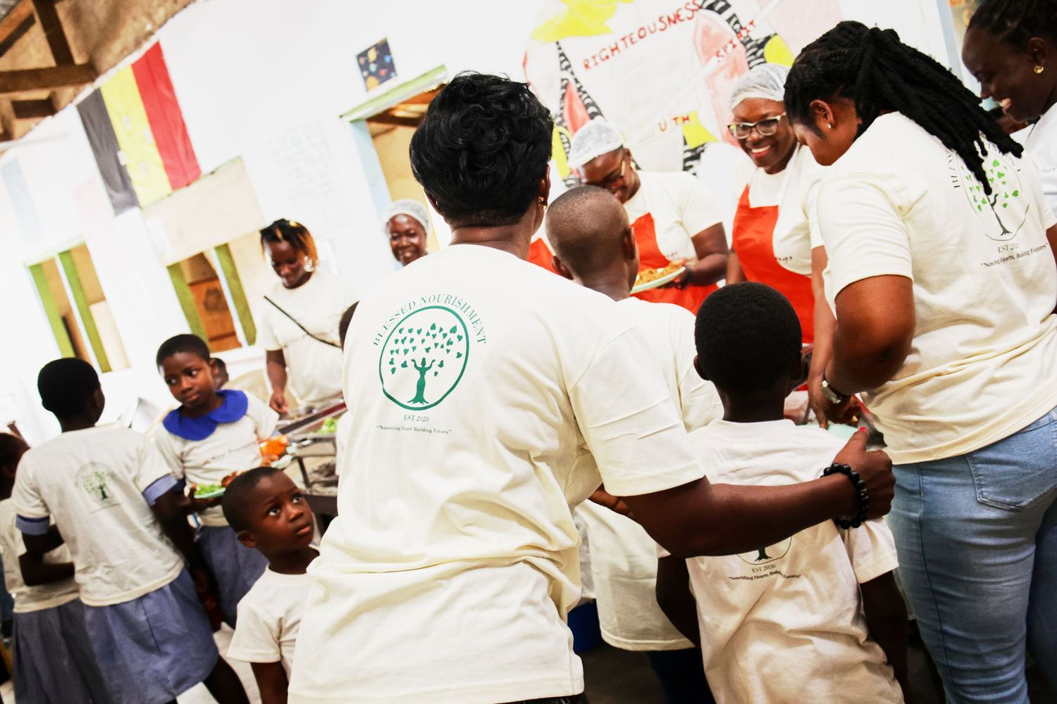 Staff members in uniforms serving food to students in a busy school cafeteria.