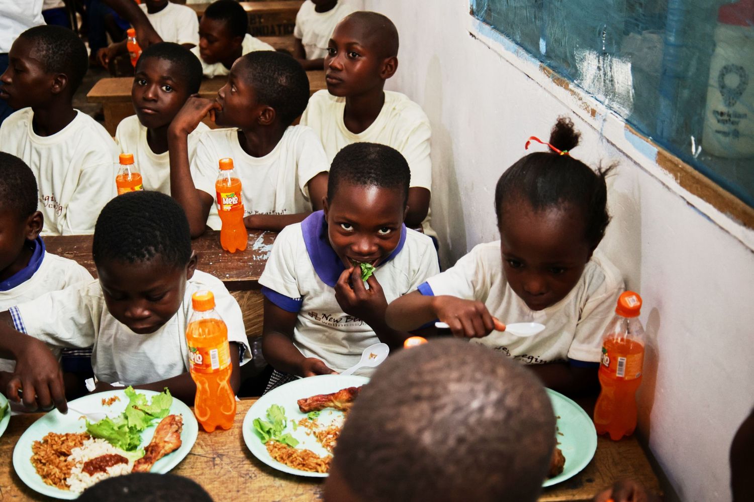Students enjoying lunch with orange drinks and plates of food in a school cafeteria.