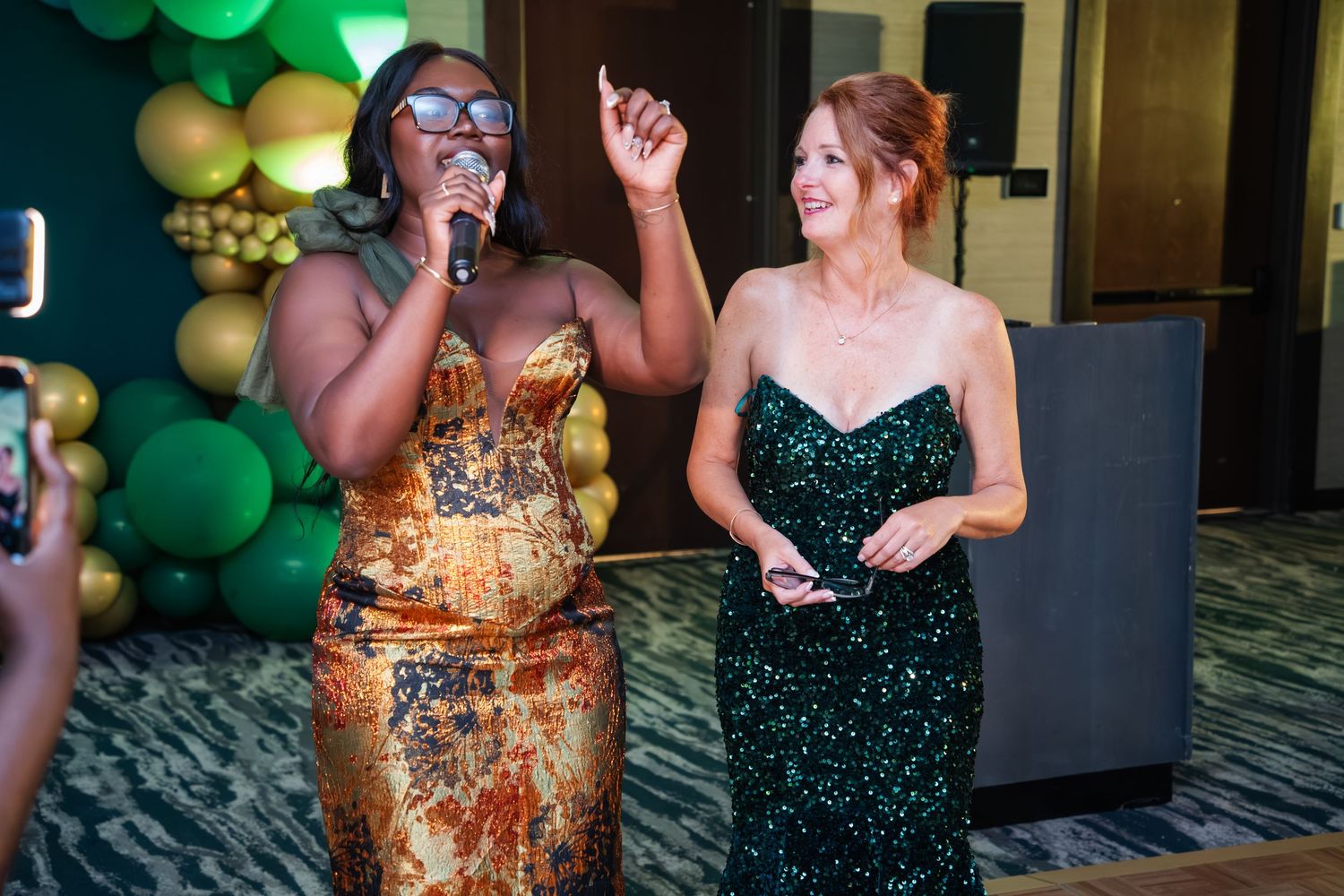 People dancing and celebrating at a formal event with green balloon decorations in the background.
