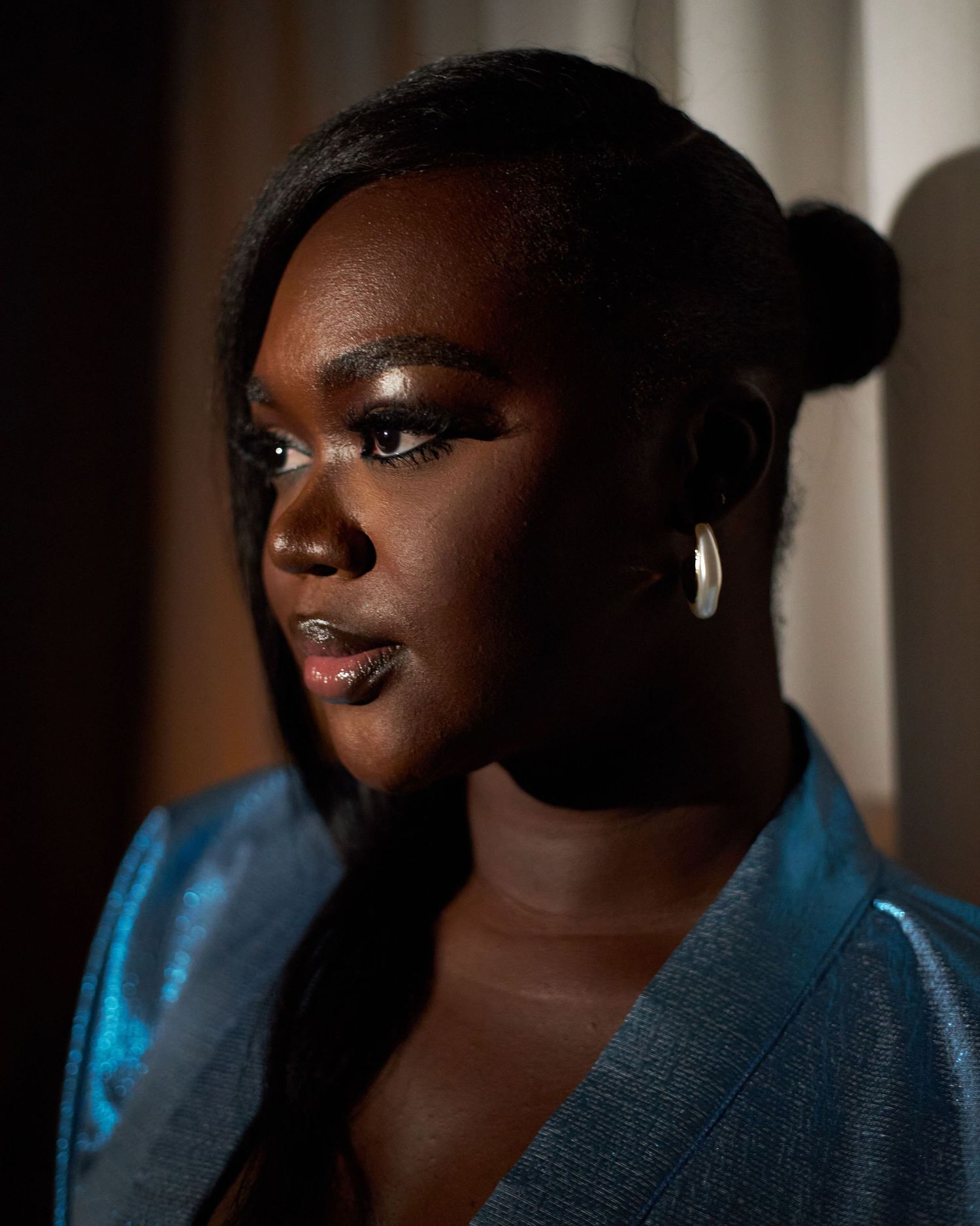 Artistic portrait with dramatic side lighting showcasing blue satin clothing against a dark background.