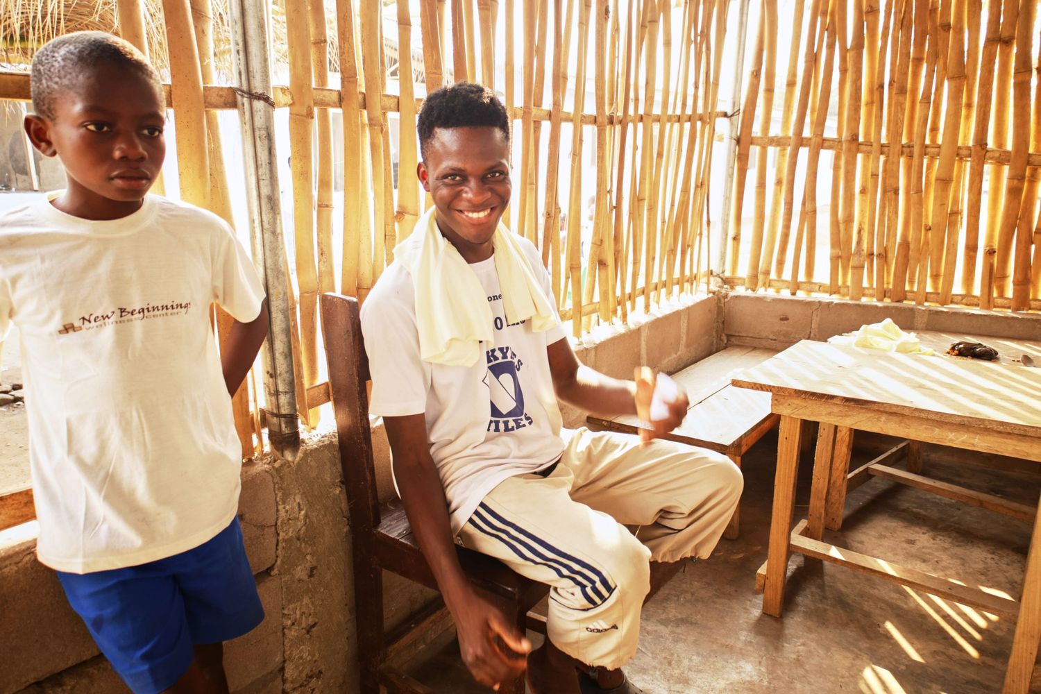Students in white shirts sit together in bamboo-walled classroom during learning activities.