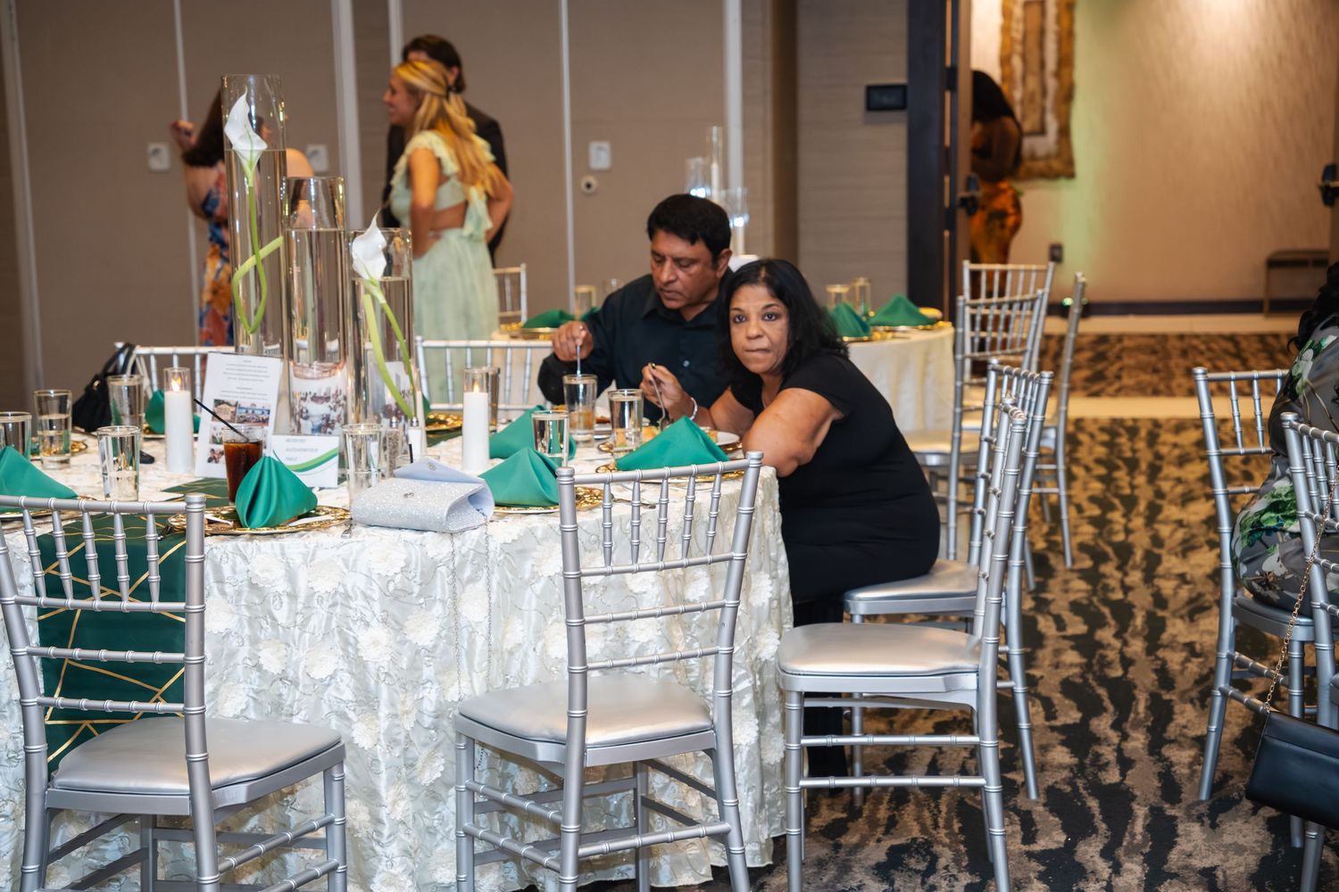 A formal event space with silver chiavari chairs and elegant table settings arranged in rows for a celebration.