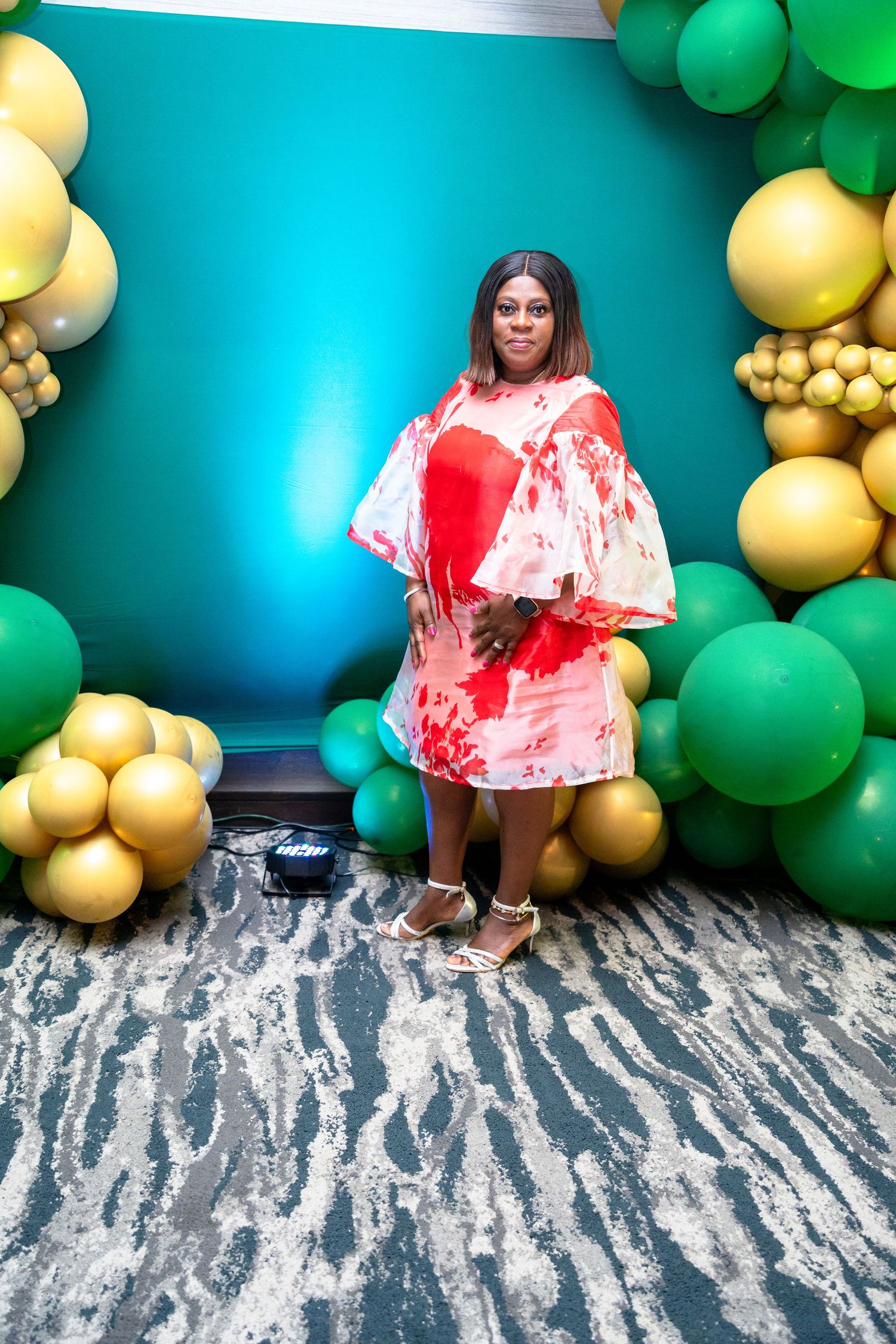 A festive party backdrop with green and gold balloons against a turquoise wall and textured floor decor.