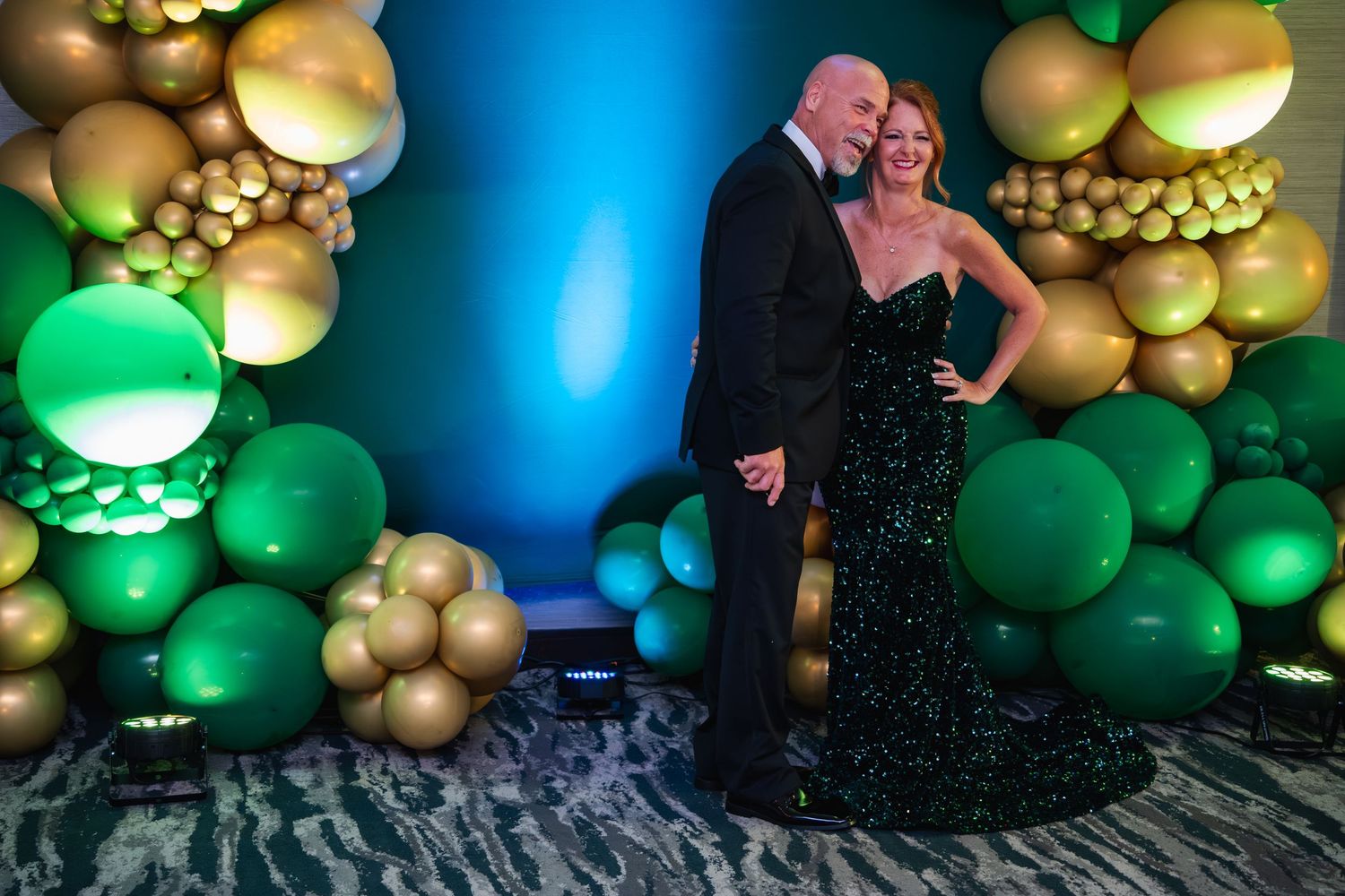 Festive balloon arch display featuring green and gold balloons against a blue-lit backdrop for an elegant party setting.