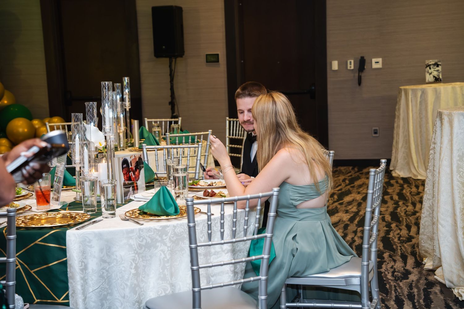 Event guests seated at an elegant table with silver chiavari chairs and white tablecloths at a formal reception.
