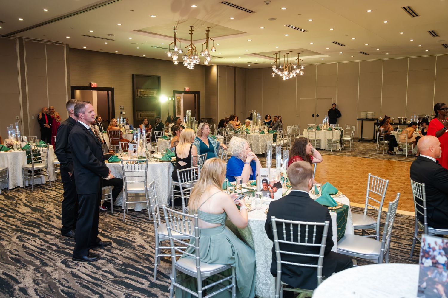 Elegant wedding reception venue setup with white chiavari chairs and crystal chandeliers in a spacious ballroom.