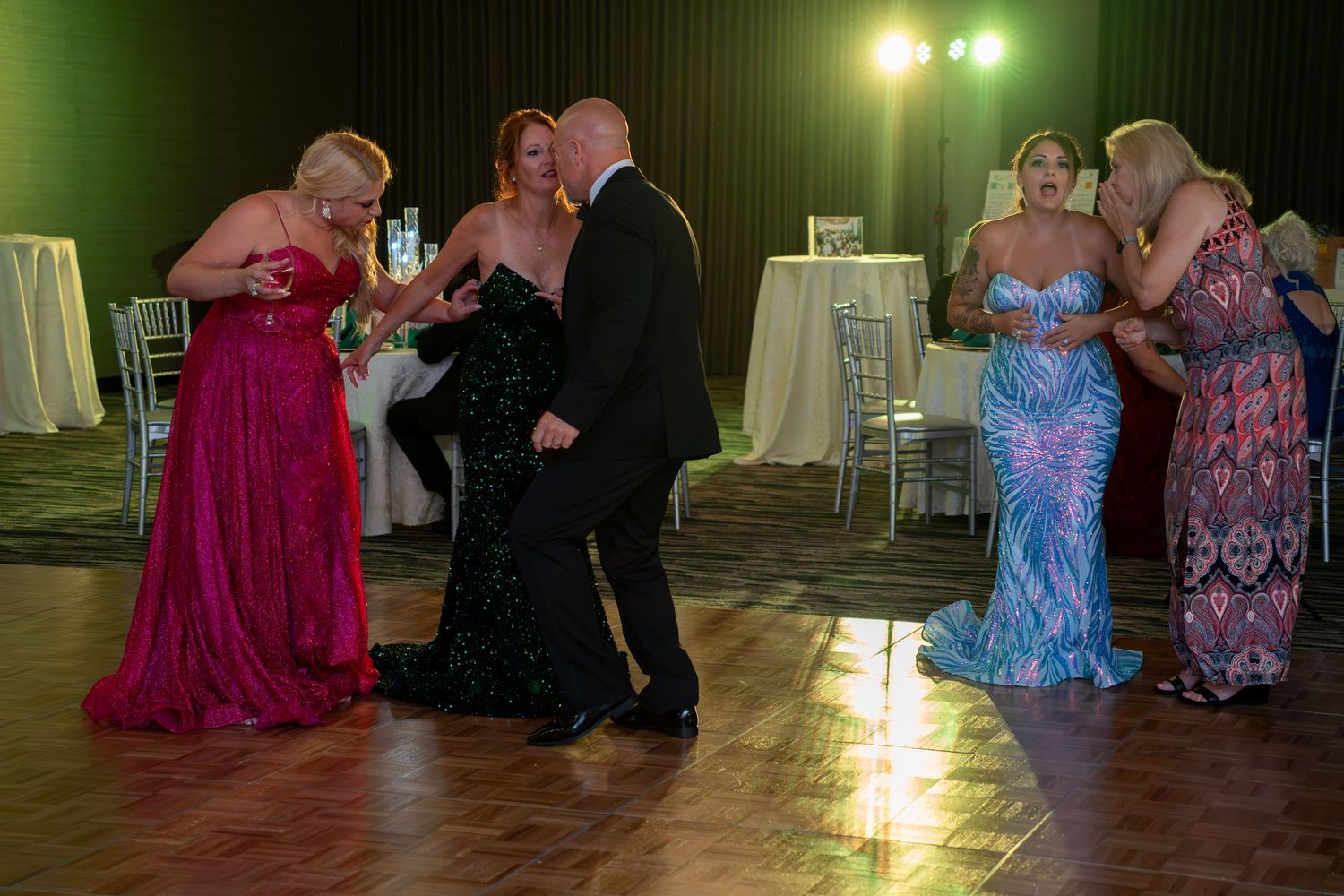 People dancing together on a wooden dance floor at an evening event with glowing lights in the background.