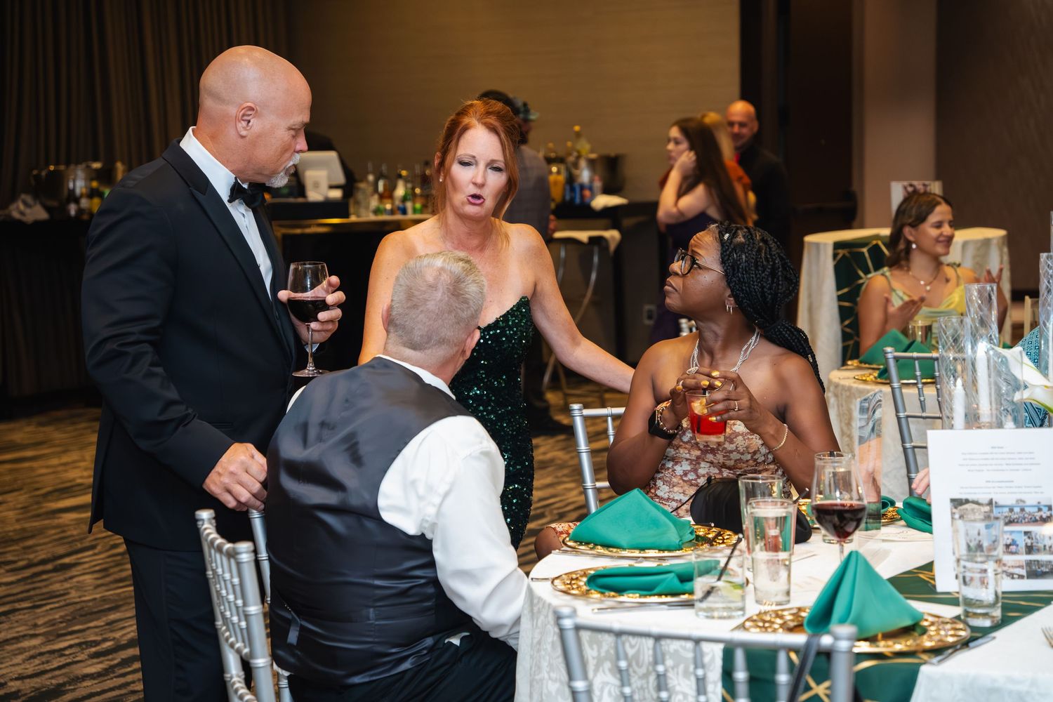 Guests enjoying conversation and dining at an elegant reception with emerald green table settings.