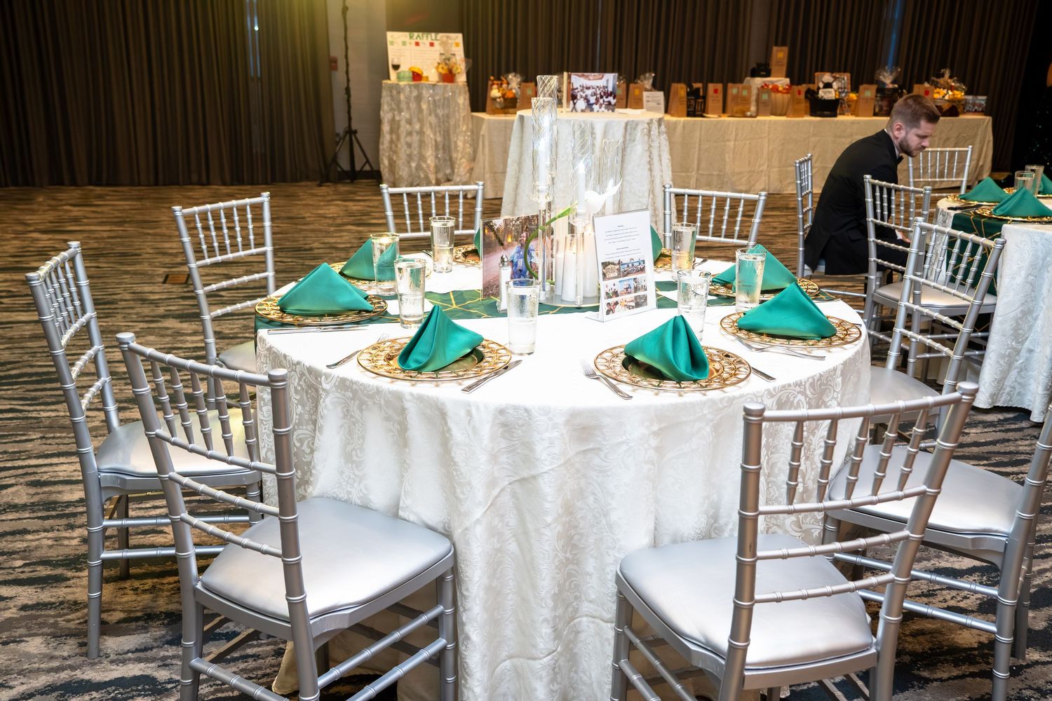 Elegant wedding reception venue with white chiavari chairs and emerald green napkins on round tables.