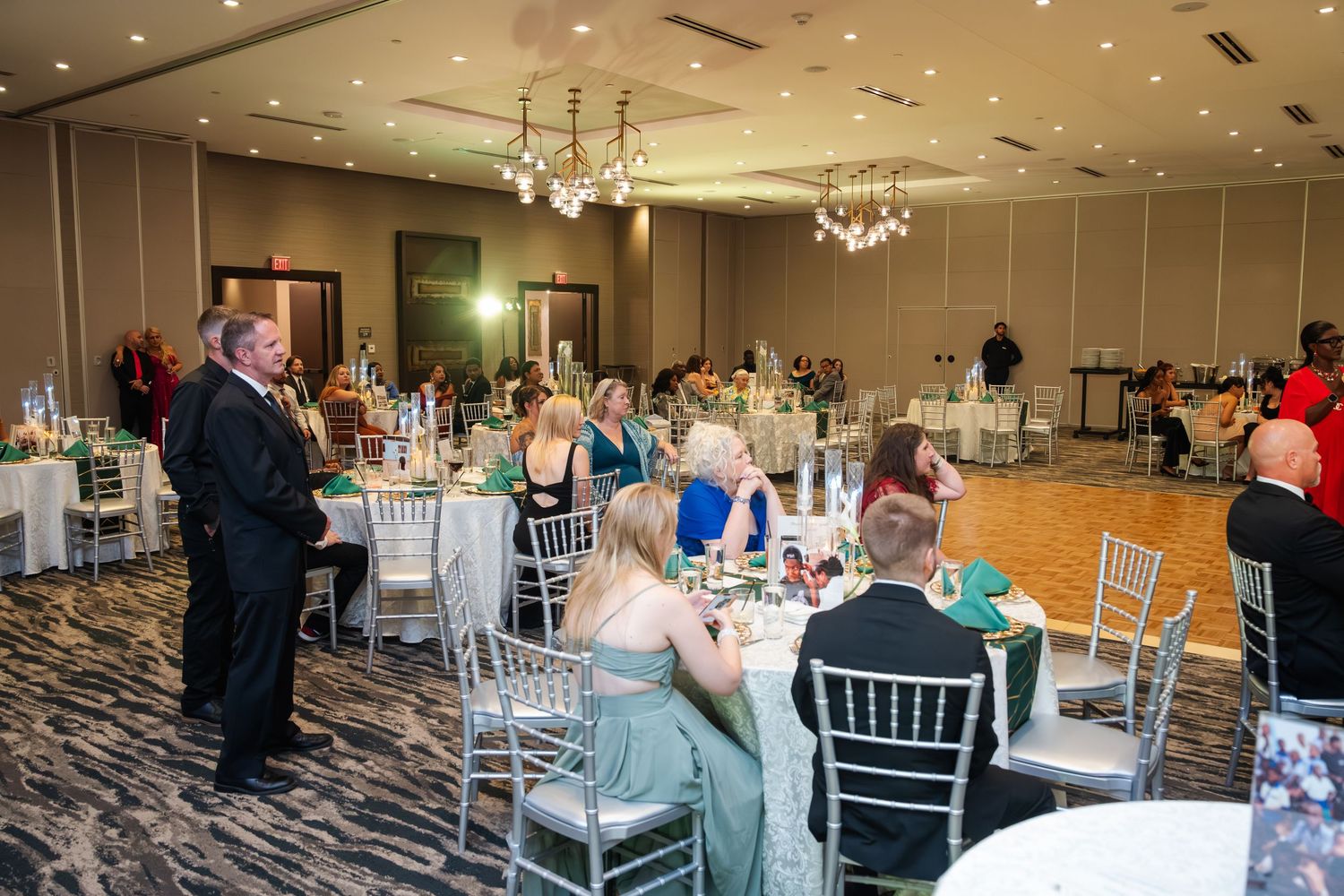 Wedding guests mingle and socialize in an elegant reception hall with crystal chandeliers and chiavari chairs.