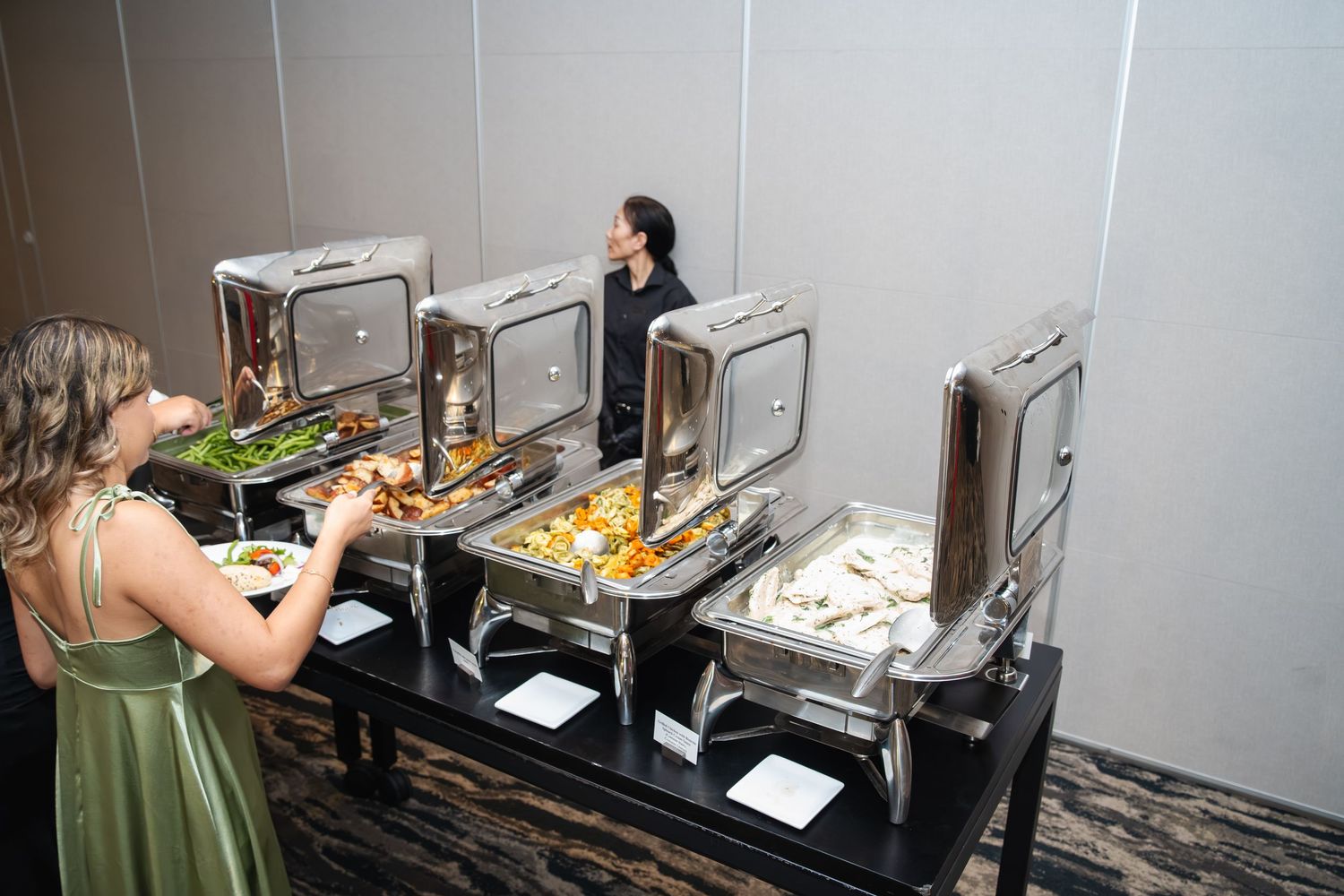 People working in a commercial kitchen preparing food at multiple stainless steel prep stations and cooking areas.