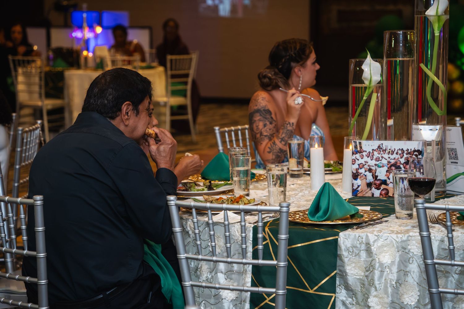 People gathered at an elegant banquet with white tablecloths and gold chairs in a formal dining setting.