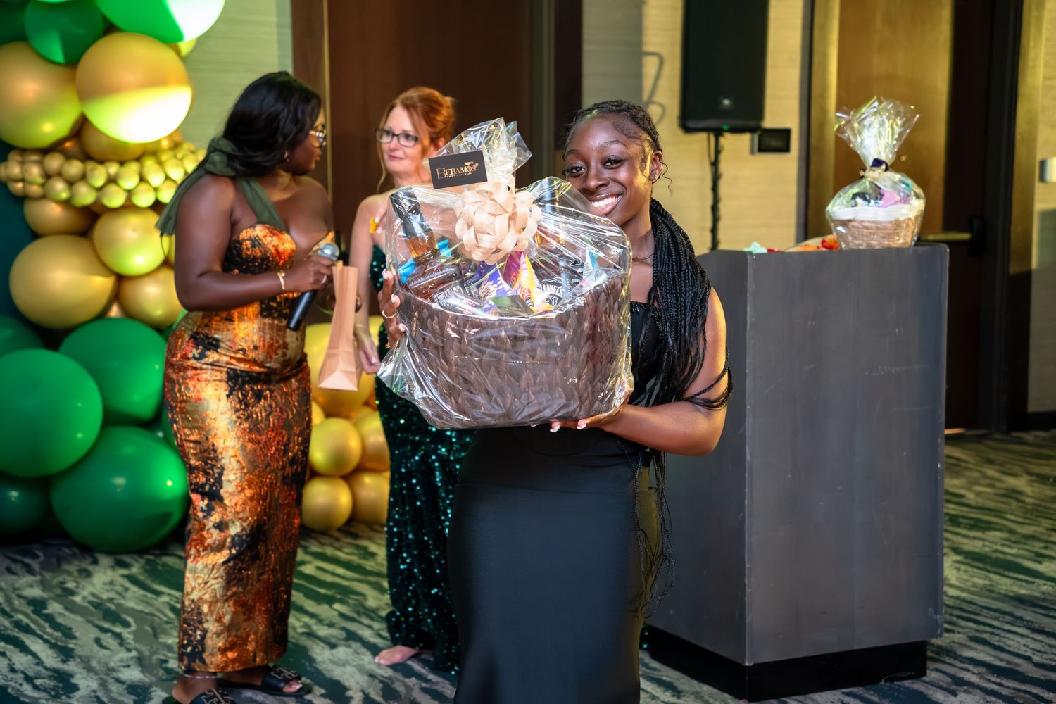 A person holding a large trophy award at an event with green and gold balloon decorations in the background.