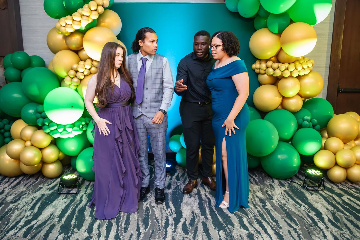 A festive balloon arch with green and gold balloons creates a backdrop for people posing at a special event.