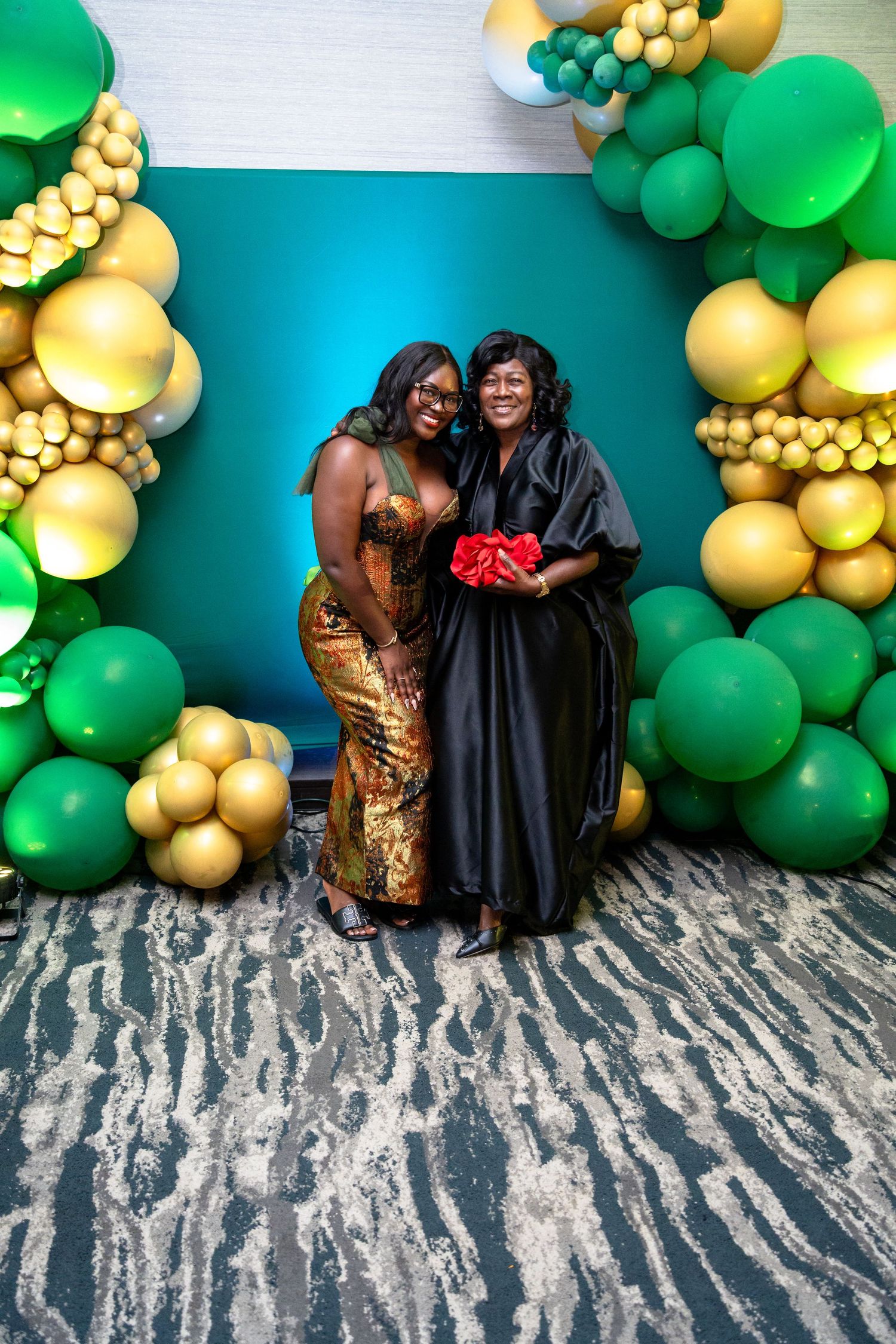 Decorative balloon arch with green and gold balloons against a turquoise wall with zebra print carpet.