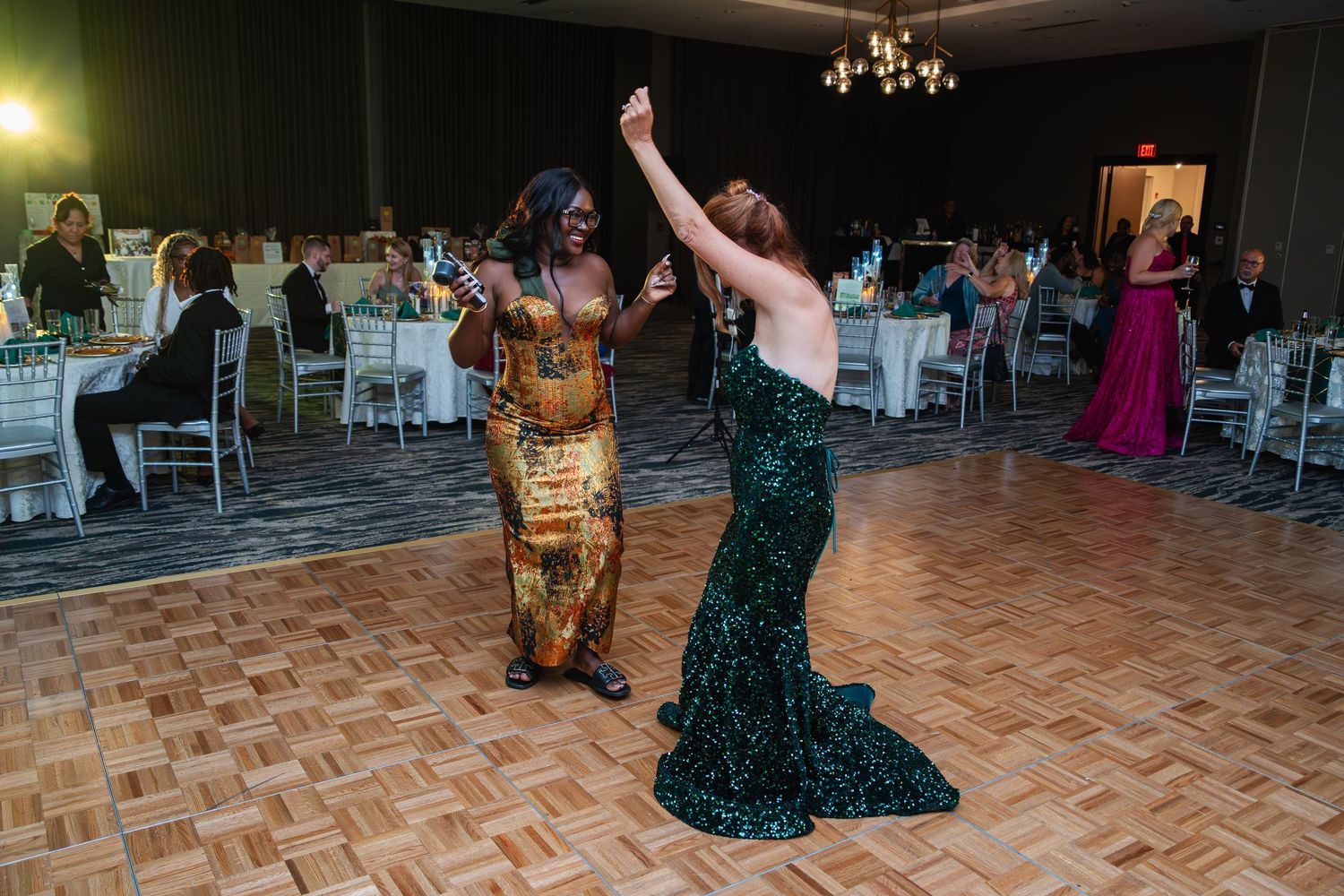 A group of people dancing on a patterned dance floor at an elegant evening event with chandeliers overhead.