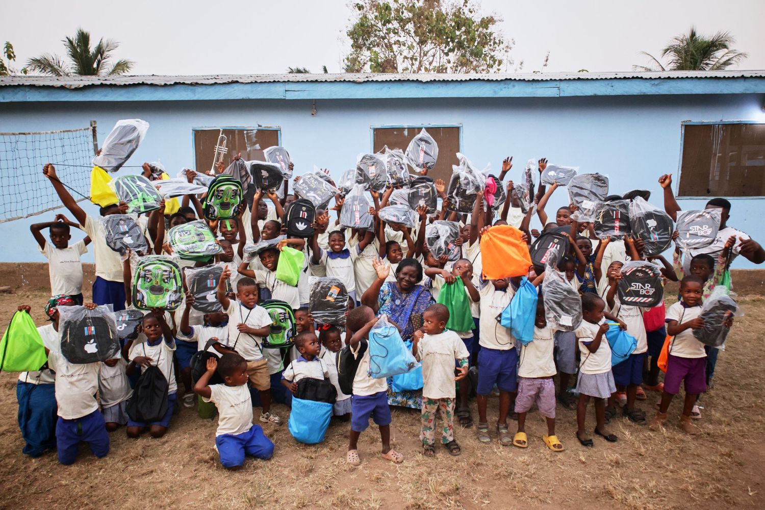 Large group of excited students with water buckets gathered outside a blue building in Africa.