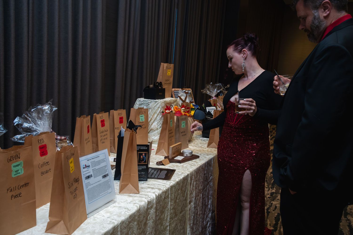 Customers participate in a whiskey tasting event with brown paper bags and glasses lined up on a wooden bar counter.