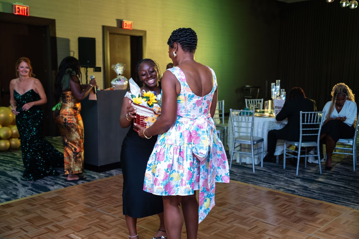 People dancing and celebrating at an indoor event venue with white chairs visible in the background.