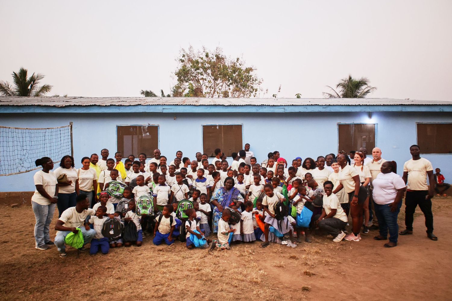 Large group photo of students and staff posed together outside a light blue building.