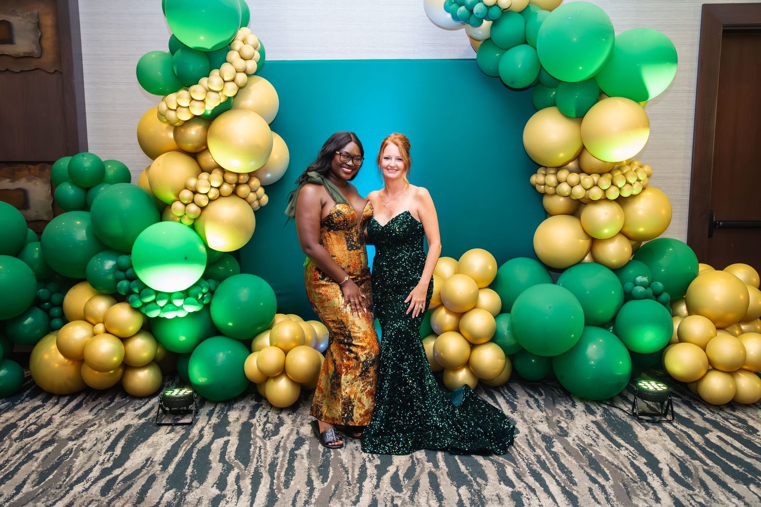 Festive balloon arch display featuring green and gold balloons against a bright turquoise wall background.