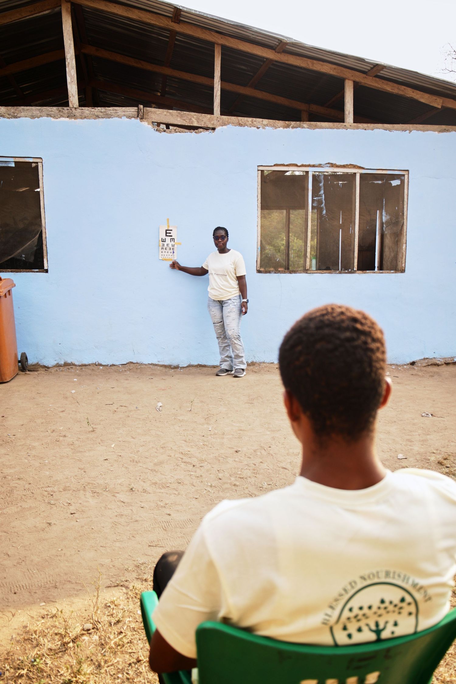 Person in white shirt gestures while teaching in front of a blue painted building.