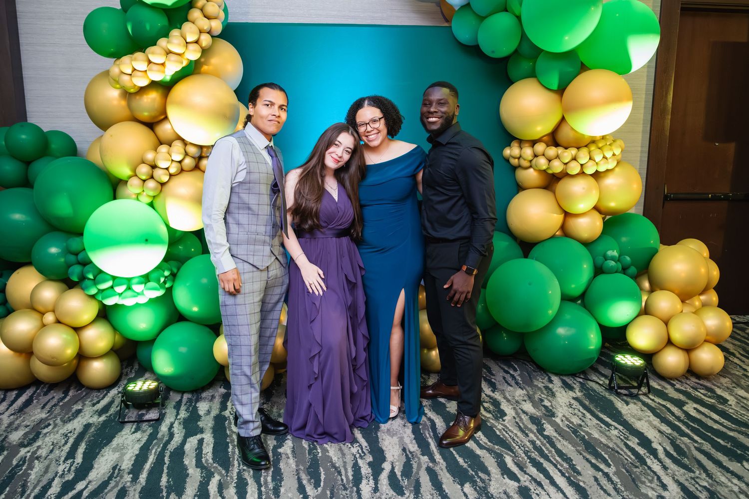 A group poses together at an event in front of a decorative green and gold balloon arch backdrop.