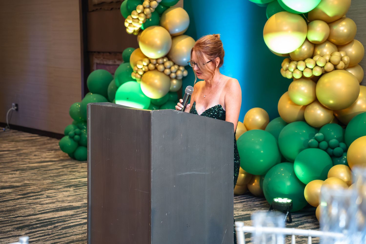 A festive balloon arch installation in progress with green and gold balloons being arranged against a wall.