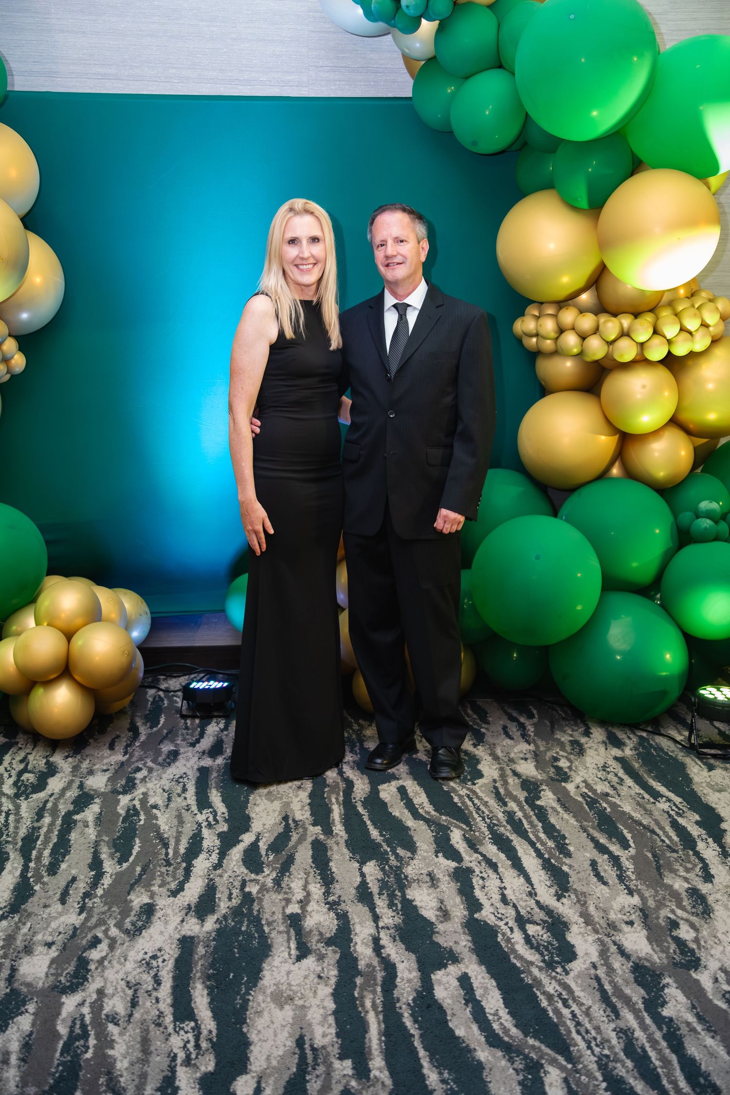 Formal event backdrop featuring green and gold balloon decorations against a blue wall.