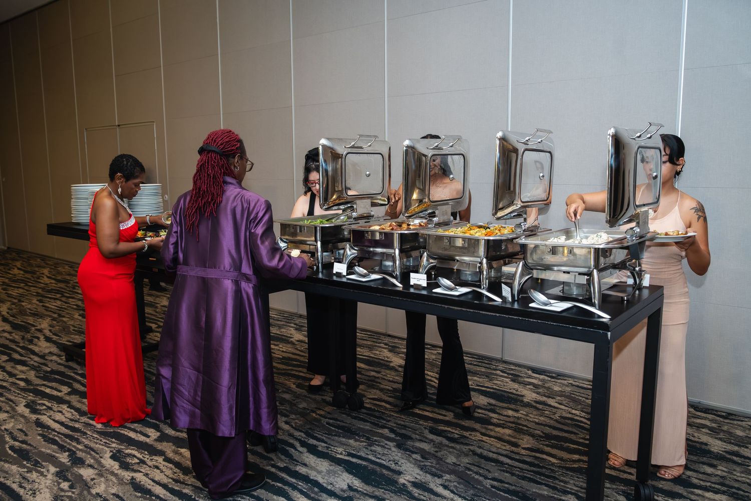 People serving themselves at a buffet line with various dishes and warming trays in a banquet setting.