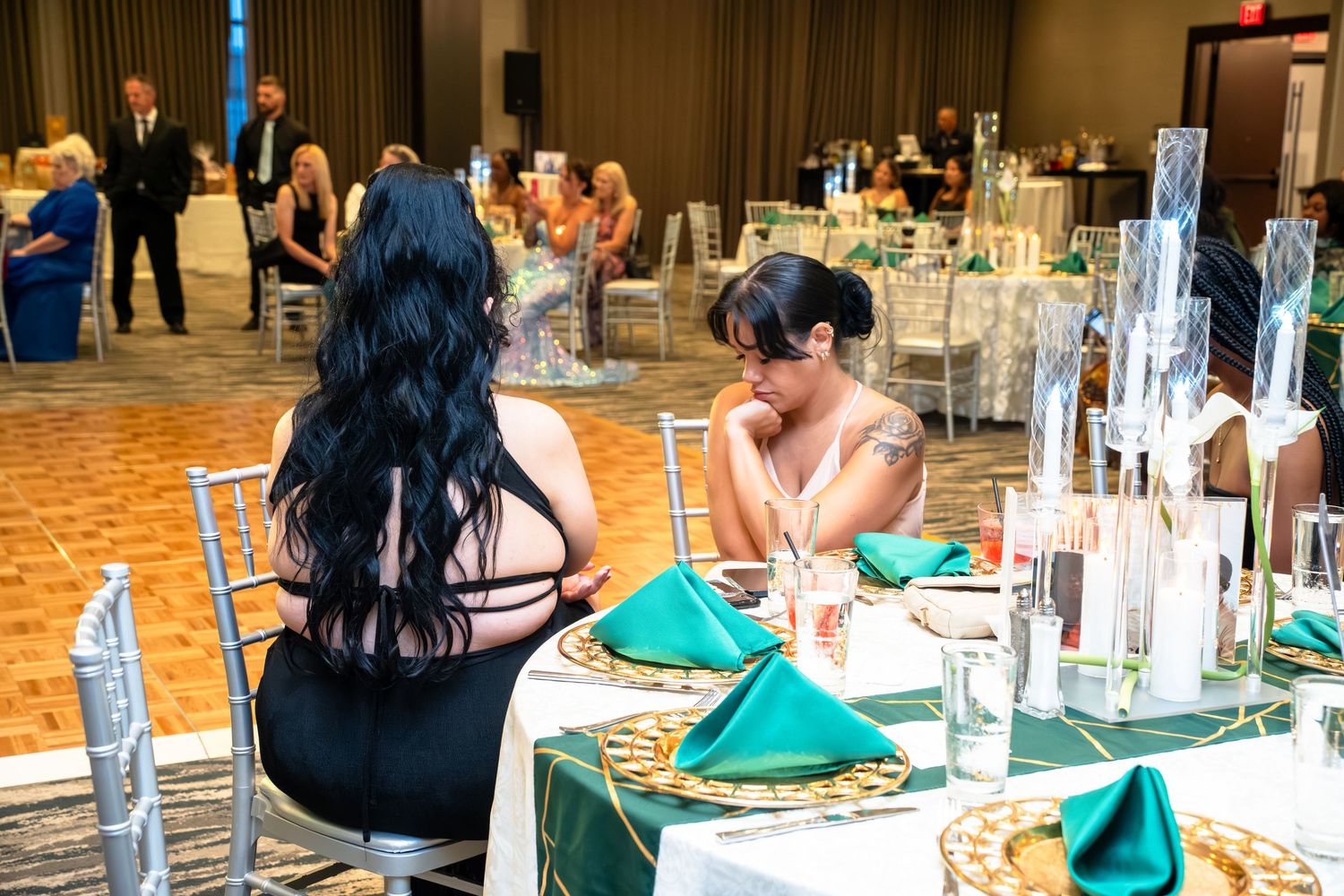 Wedding reception tables decorated with emerald green linens and elegant place settings in a grand ballroom.