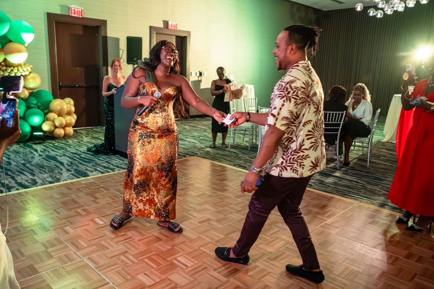 People dancing together in a ballroom with green lighting and patterned floor tiles.