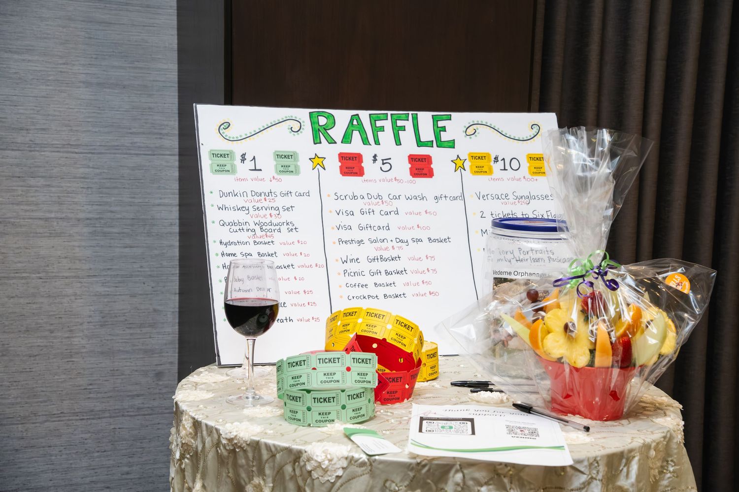A colorful raffle display with tickets, prizes and handwritten signs arranged on a dark tablecloth.