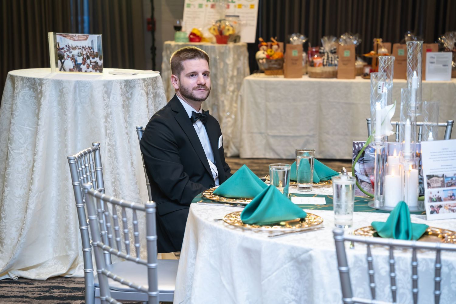 Elegant wedding reception setup with silver chiavari chairs and teal napkins at round tables in a formal venue.