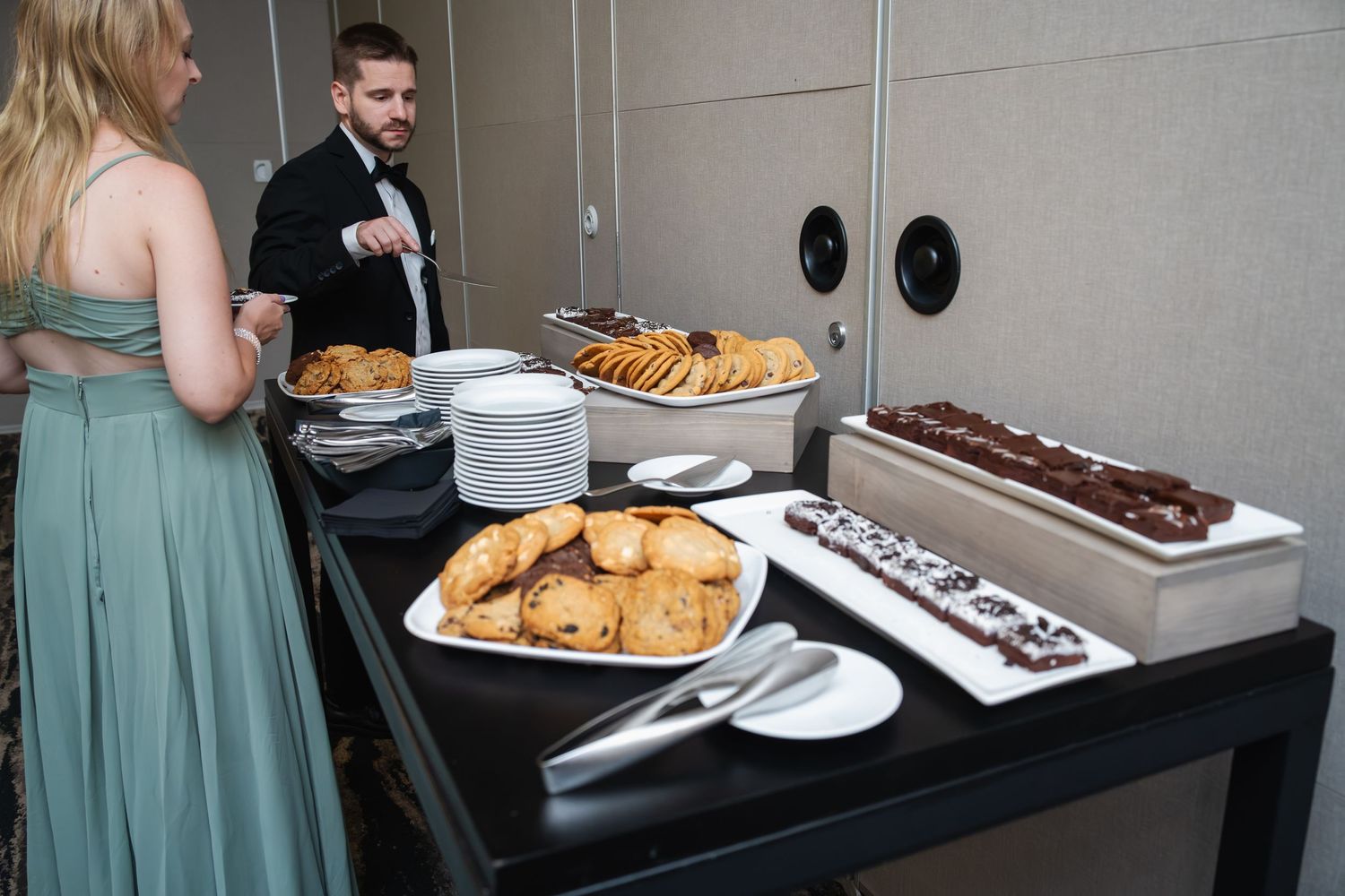 A dessert and refreshment table at an event displays platters of cookies, pastries and other sweet treats.