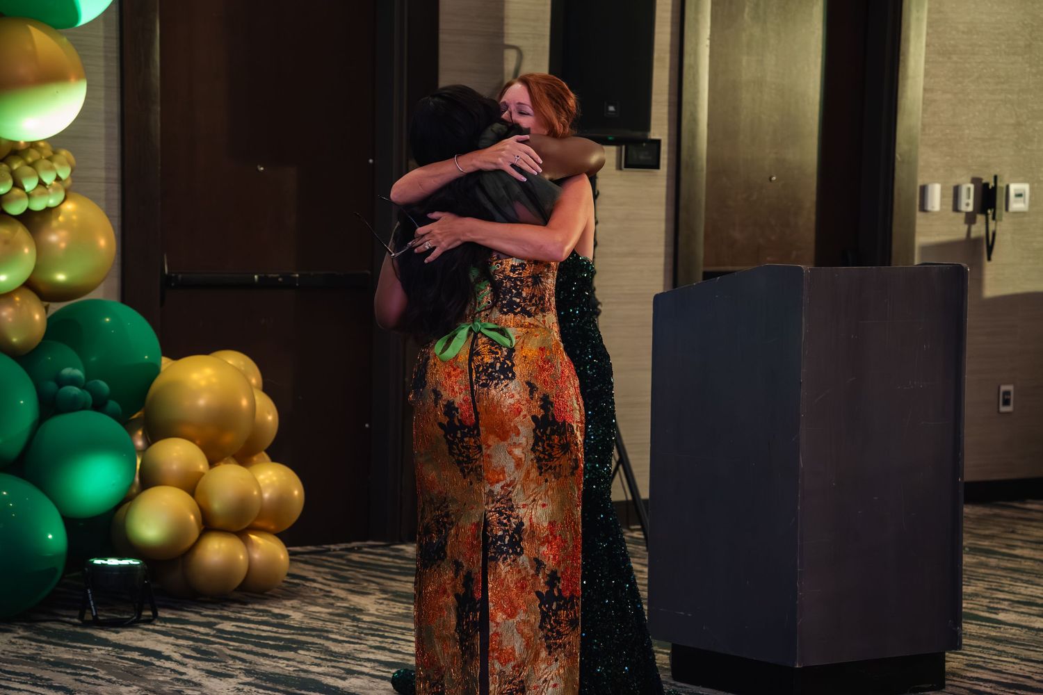 A festive event space decorated with green and gold balloon arrangements along a wall.