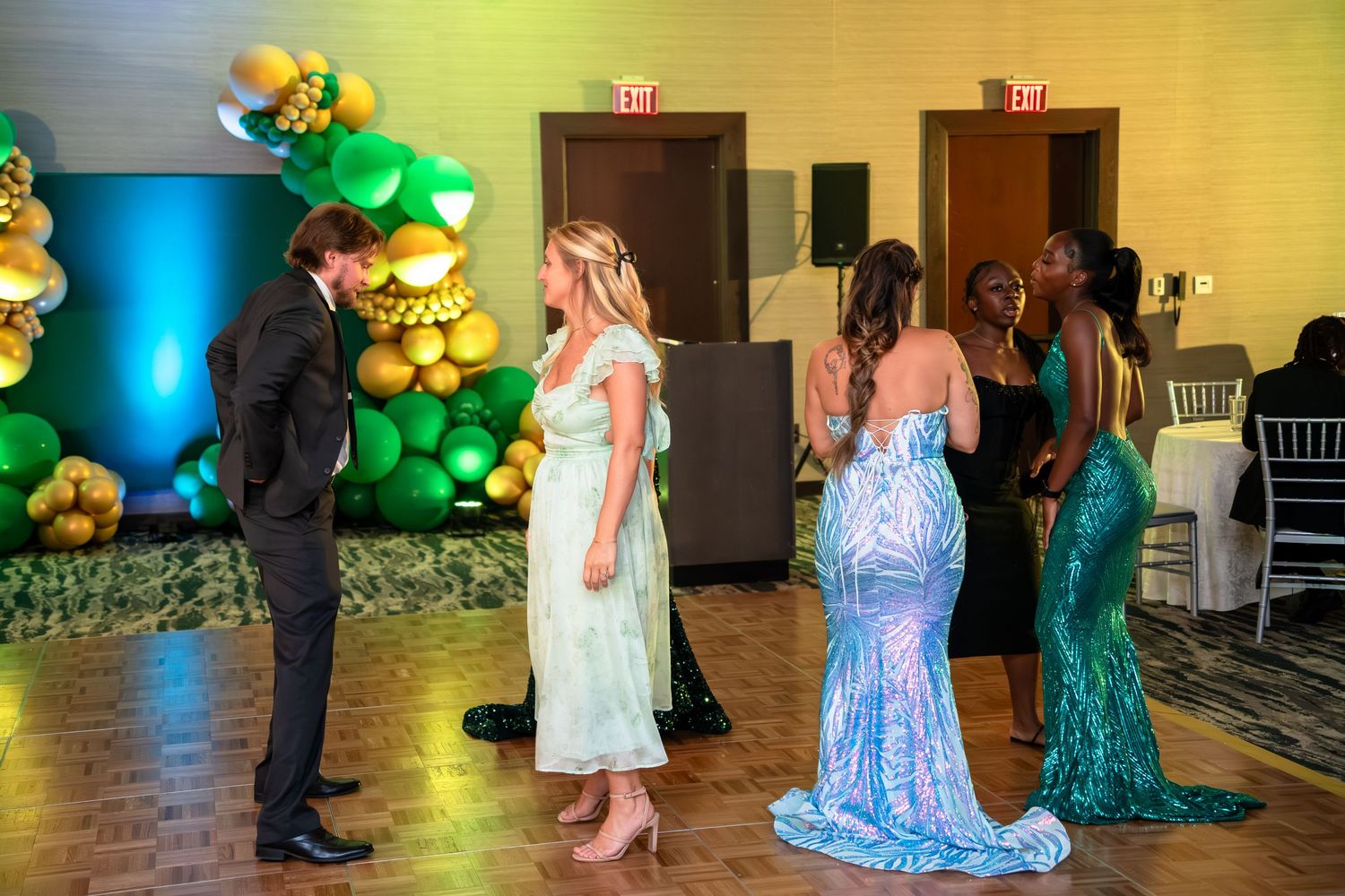 People dancing at an event with gold balloon decorations and turquoise lighting in a banquet hall.