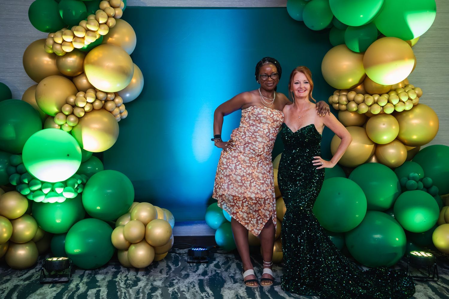 Festive balloon arch installation with green and gold balloons creates an elegant party backdrop against a blue wall.