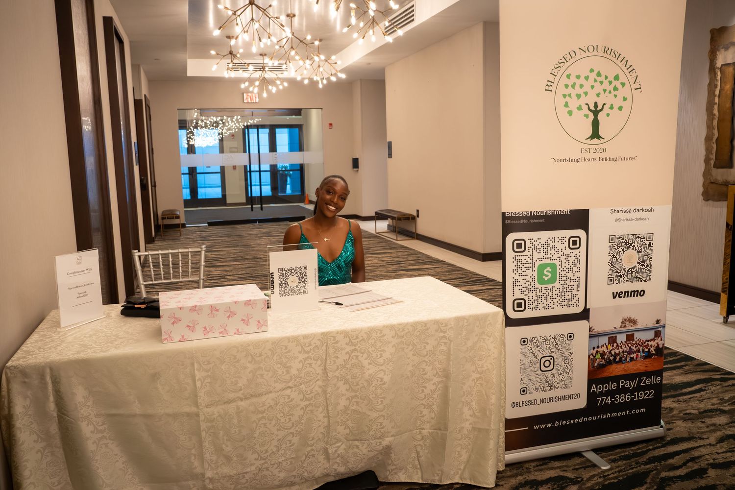Elegant event venue with crystal chandeliers, white tablecloths, and decorative tree artwork displayed on the walls.